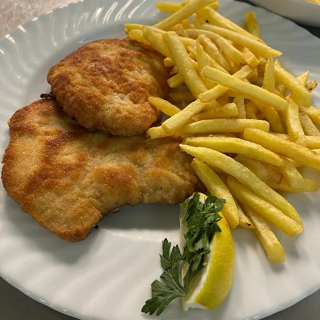 Panierte Schnitzel mit Pommes frites, Zitronenschnitz und Petersilienzweig auf weißem Teller