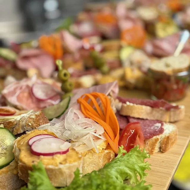 Verschiedene belegte Brotscheiben mit Salat, Gurke, Radieschen, Karottenstreifen, Zwiebeln und Aufschnitt auf Holzbrett angerichtet.