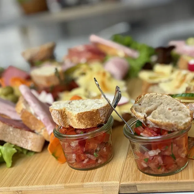 Verschiedene belegte Brotscheiben auf Holzbrett mit kleinen Gläsern Tomatensalsa und Besteck