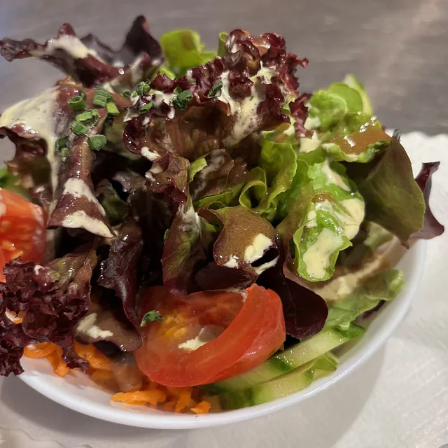 Schüssel mit grünem und rotem Blattsalat, Tomatenscheiben, Gurkenstreifen, geraspelten Karotten und cremigem Dressing